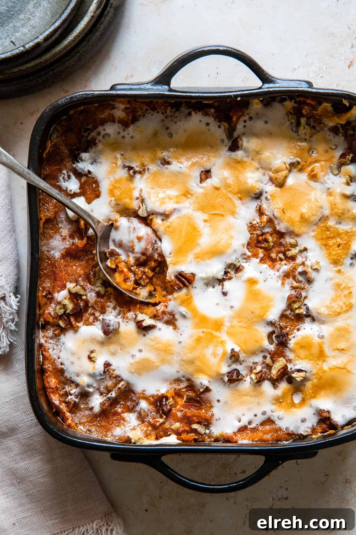 A serving spoon resting in a square black baking dish of sweet potato casserole.