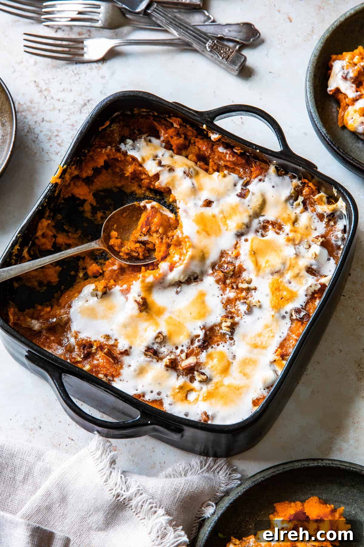 A square black baking dish filled with sweet potato casserole, topped with golden-brown melted marshmallows.