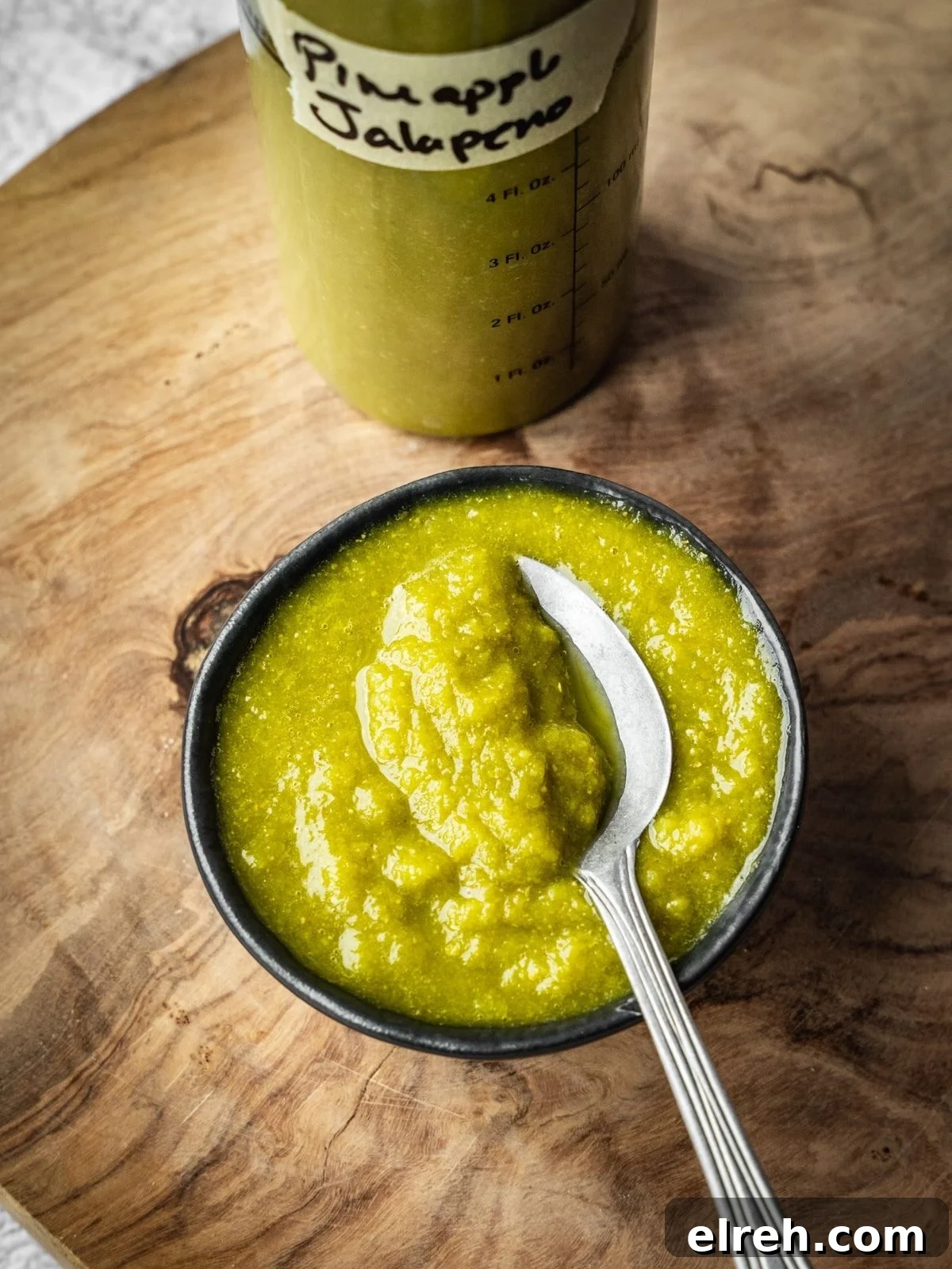 Fermented Pineapple Jalapeno Hot Sauce Recipe 8 A small bowl of pineapple jalapeno hot sauce with a bottle on a wooden board.