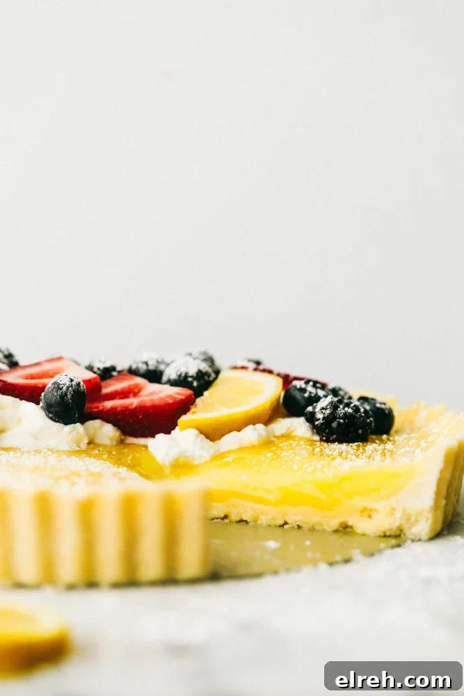 Lemon tart photo of a side of the dessert with fresh berries on top and powdered sugar. 