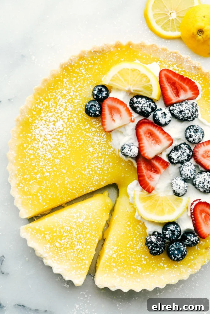 Lemon tart photo with fresh berries on top with lemon slices and powder sugar sprinkled on top and a slice cut out of the tart. 