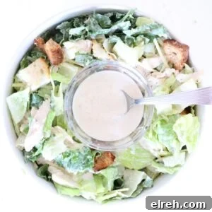 One bowl of Caesar salad with a small glass bowl of Caesar dressing with a spoon in the center.