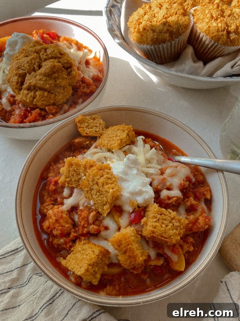 chicken chili in a bowl with cheese and sour cream and cubes of cornbread