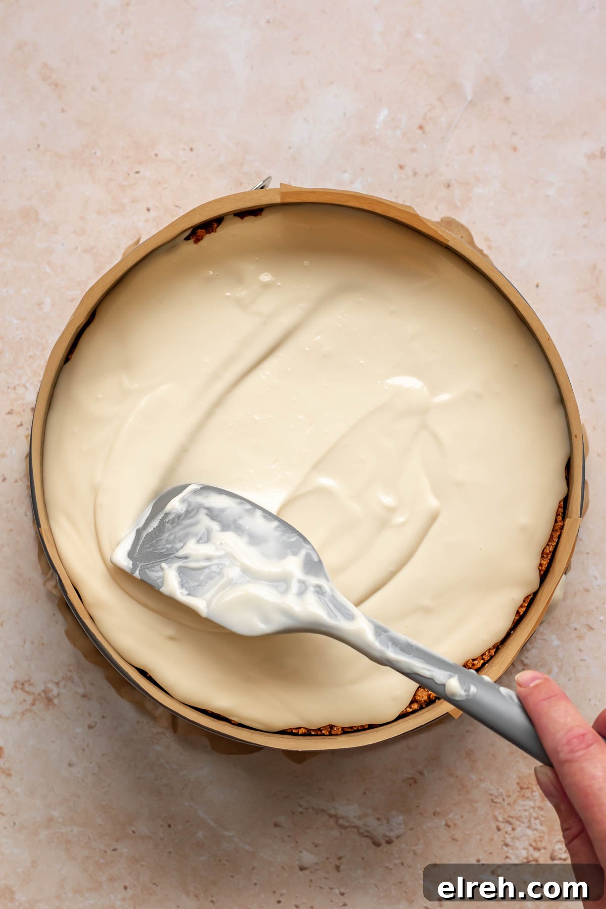 Apple Crumble Cheesecake with Cinnamon Streusel Recipe 17 A spatula spreads cheesecake batter evenly.