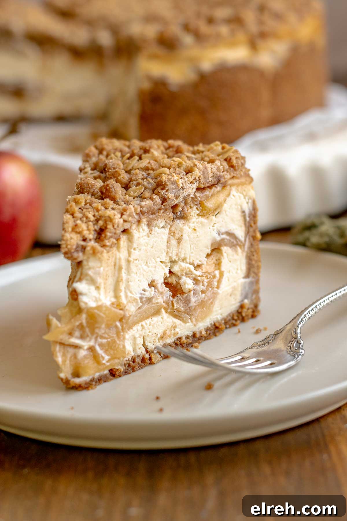 Apple Crumble Cheesecake with Cinnamon Streusel Recipe 20 A slice of apple crisp cheesecake on a plate with a fork next to it.