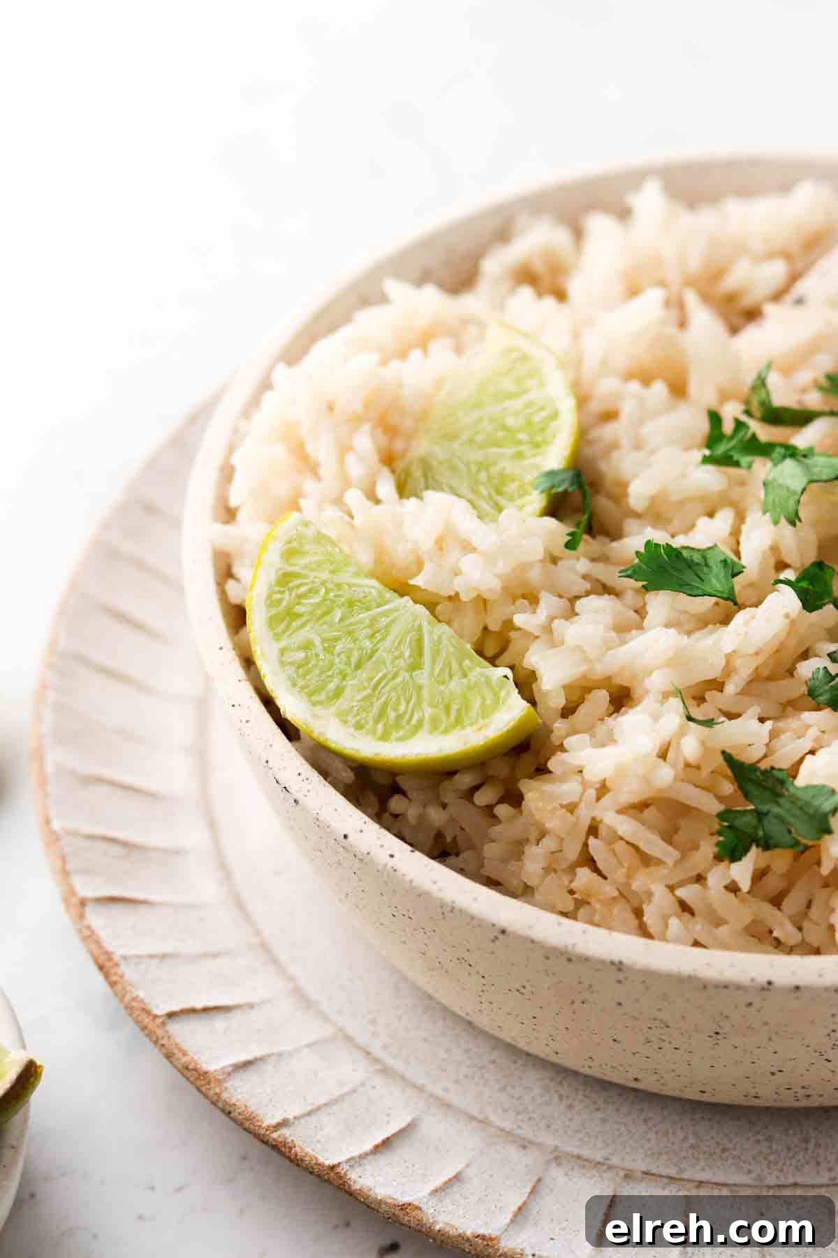 Coconut rice in a bowl with lime wedges and fresh green herbs.