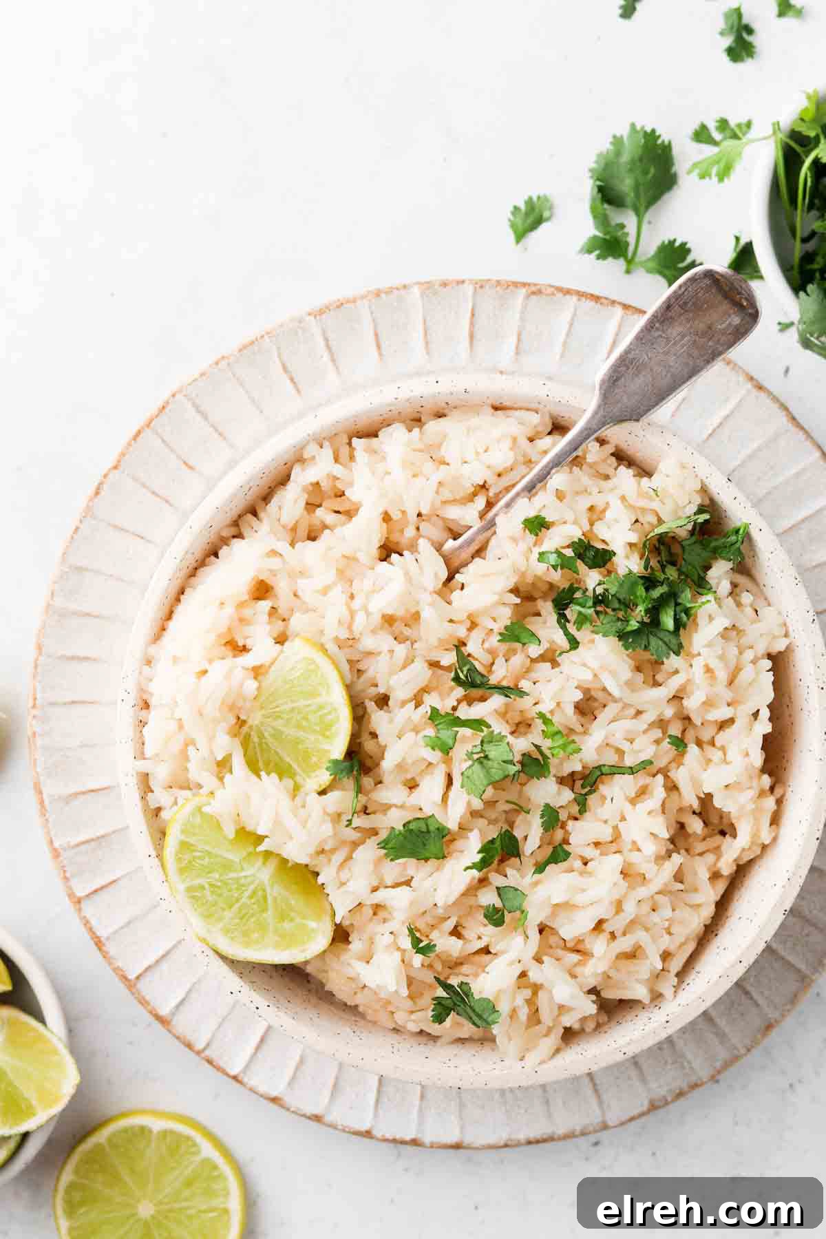 Coconut rice in a bowl with fresh limes and herbs on top.