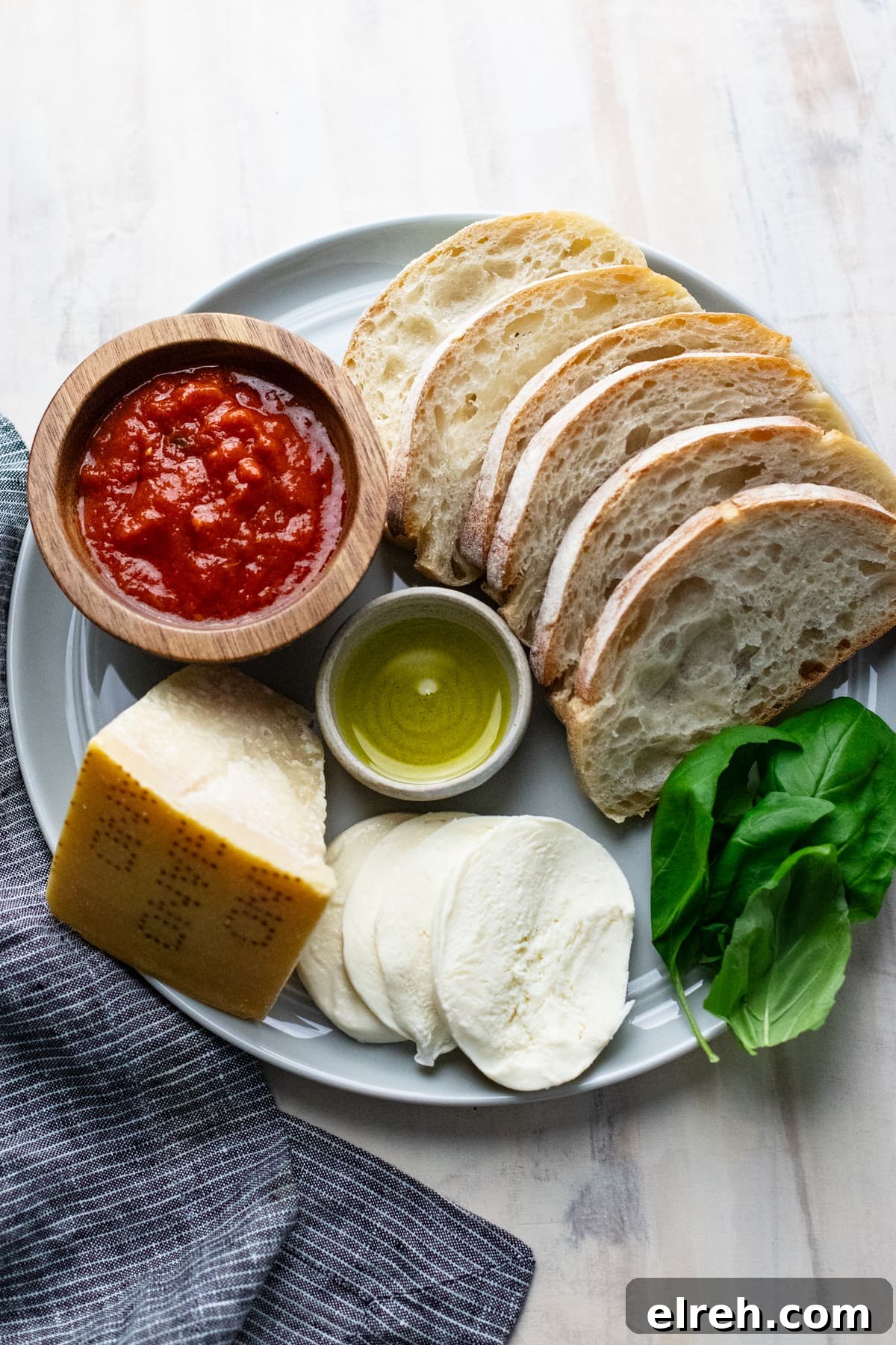 ingredients for crostini pizzas arranged on gray plate with dark napkin next to it.