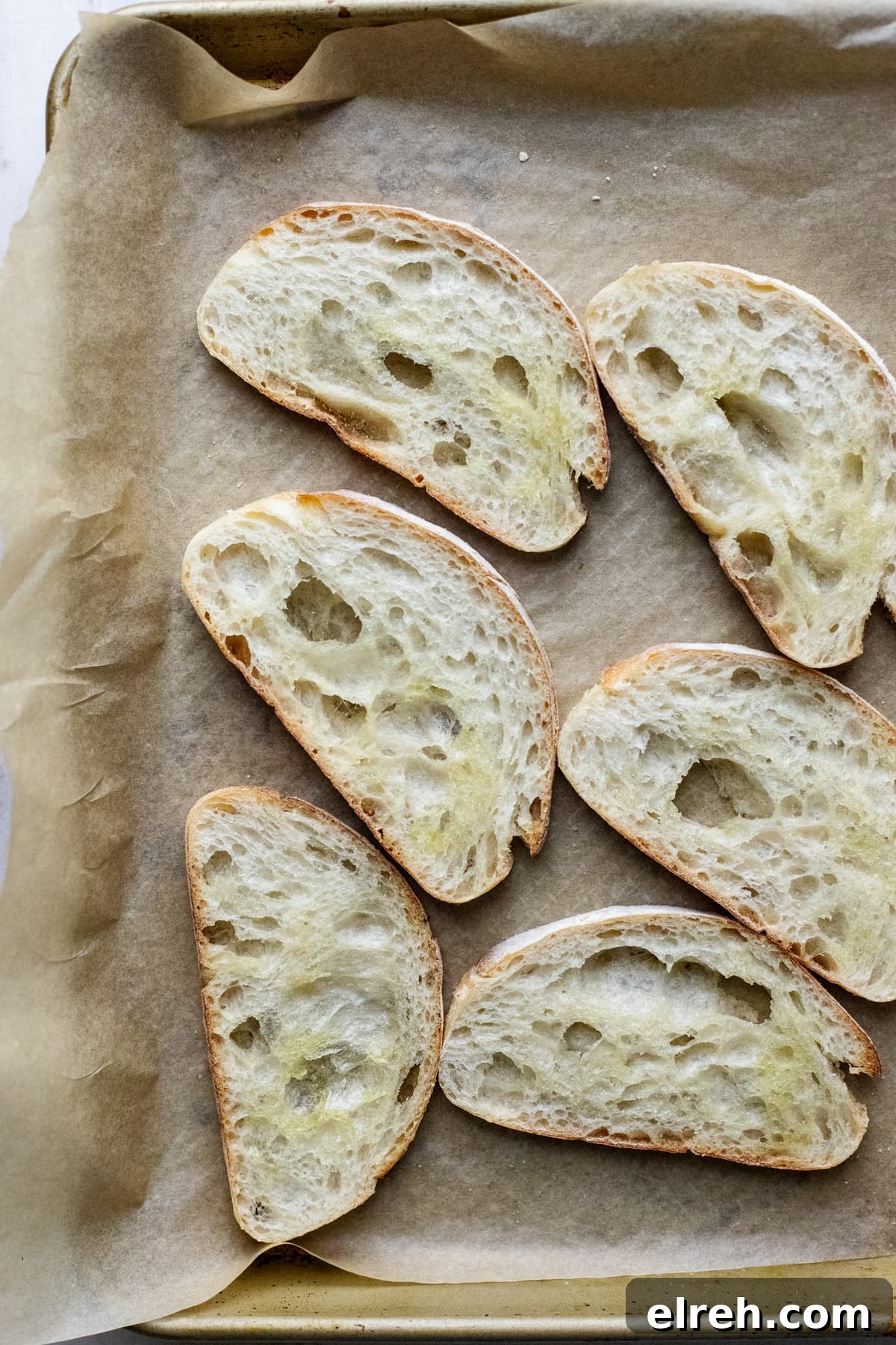 slices of ciabatta bread arranged on pan lined with parchment paper.