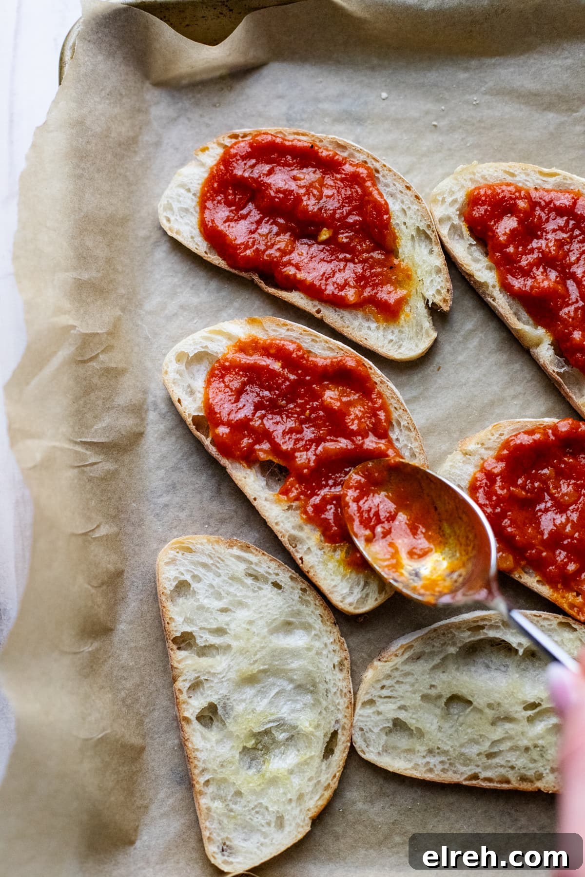 spoon spreading tomato sauce on crostini slices.