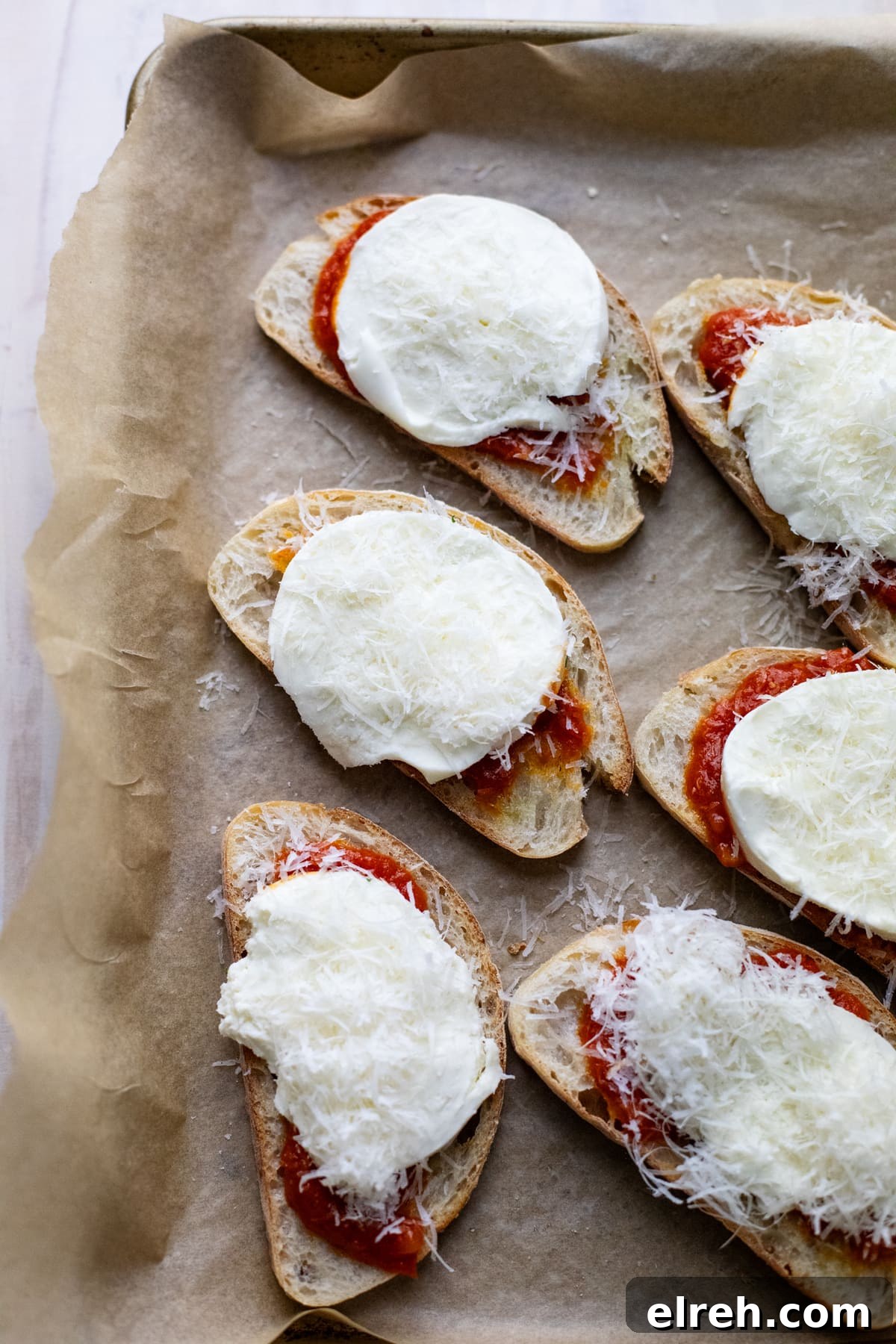 crostini pizzas arranged on pan lined with parchment paper.