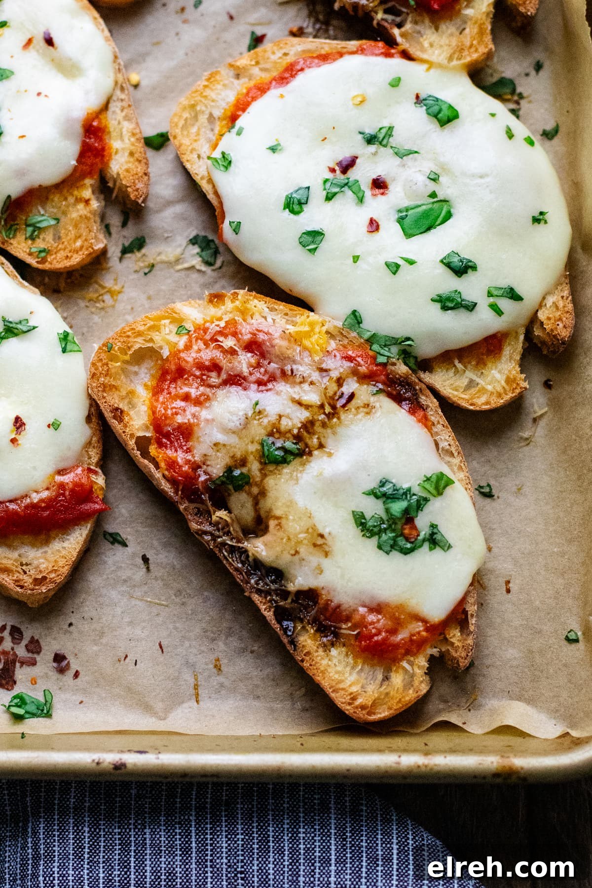 crostini pizzas arranged on baked pan lined with parchment paper and topped with chopped fresh herbs.
