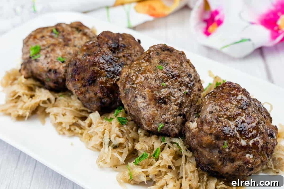 Four browned meat patties are served on a bed of shredded cooked cabbage on a white rectangular plate.
