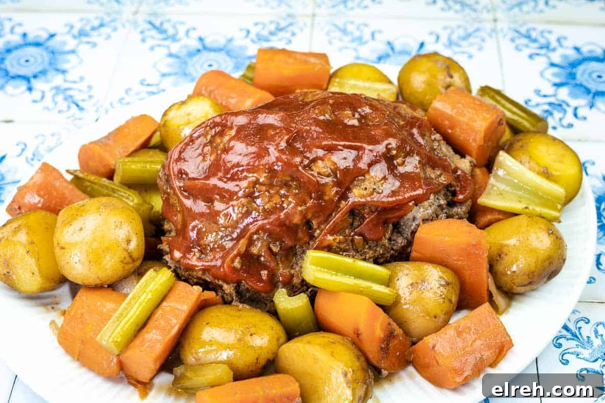 A plate of meatloaf topped with tomato sauce, surrounded by cooked baby potatoes, carrots, and celery on a patterned tile background.