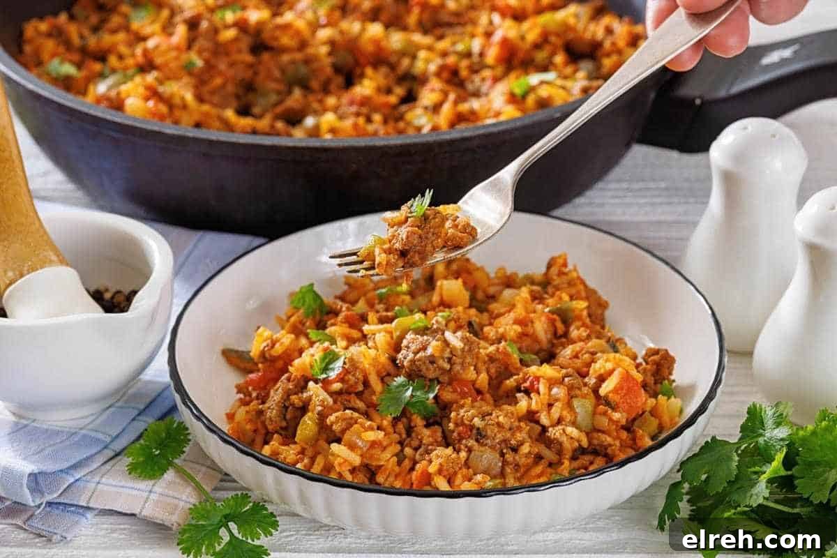 A bowl of Texas hash with rice garnished with cilantro, with a fork lifting a bite, and a skillet of the same dish in the background.