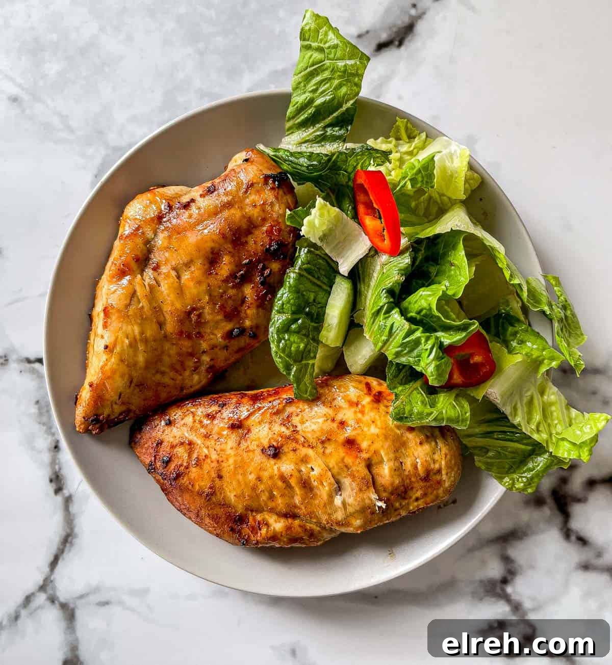 How to Cook Frozen Chicken Breasts in an Air Fryer 2 Juice air fried chicken breasts on a dinner plate with a green salad.