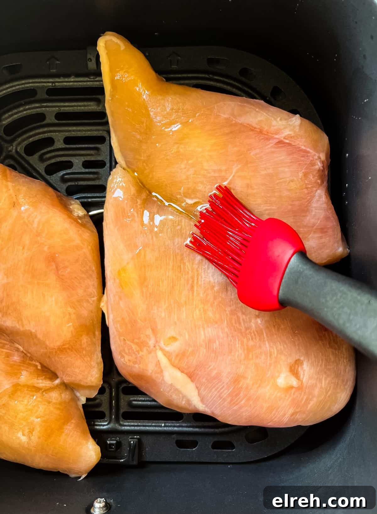 How to Cook Frozen Chicken Breasts in an Air Fryer 4 A brush applying olive oil to the top of the chicken breasts in the air fryer basket.