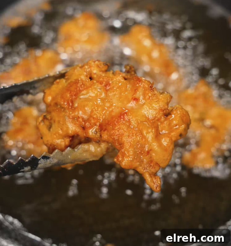 How to Make Mochiko Chicken: Crispy Hawaiian Fried Chicken 6 Golden brown mochiko chicken piece being lifted from hot oil using tongs, with other pieces bubbling in the background during deep frying.
