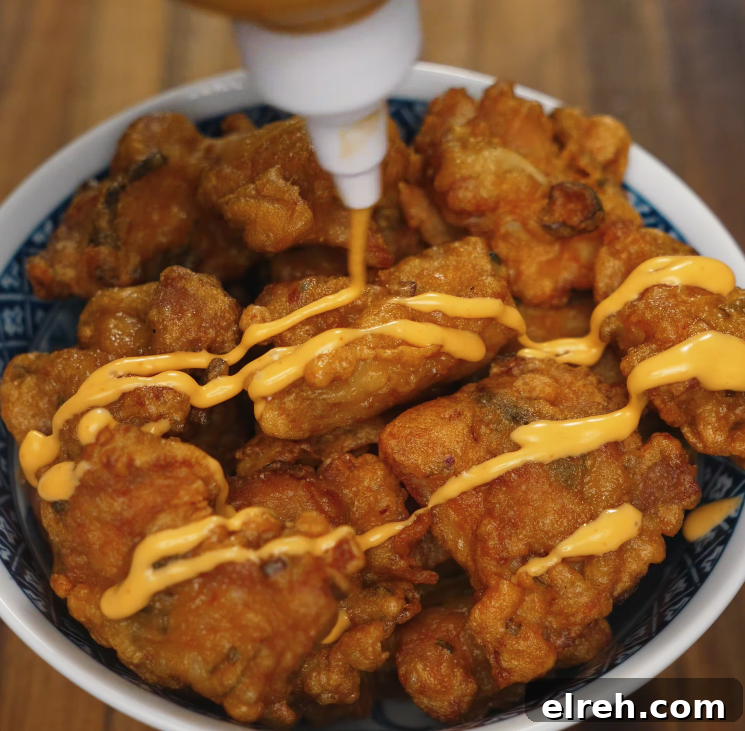 How to Make Mochiko Chicken: Crispy Hawaiian Fried Chicken 7 Spicy mayo being drizzled over a bowl of crispy mochiko chicken, adding a creamy, tangy flavor boost before garnishing.