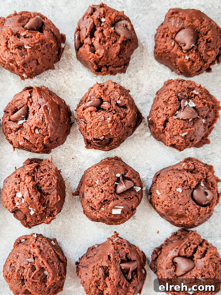 Scoops of brownie batter on a marbled surface. They are studded with chocolate chips and sprinkled with flaky sea salt.