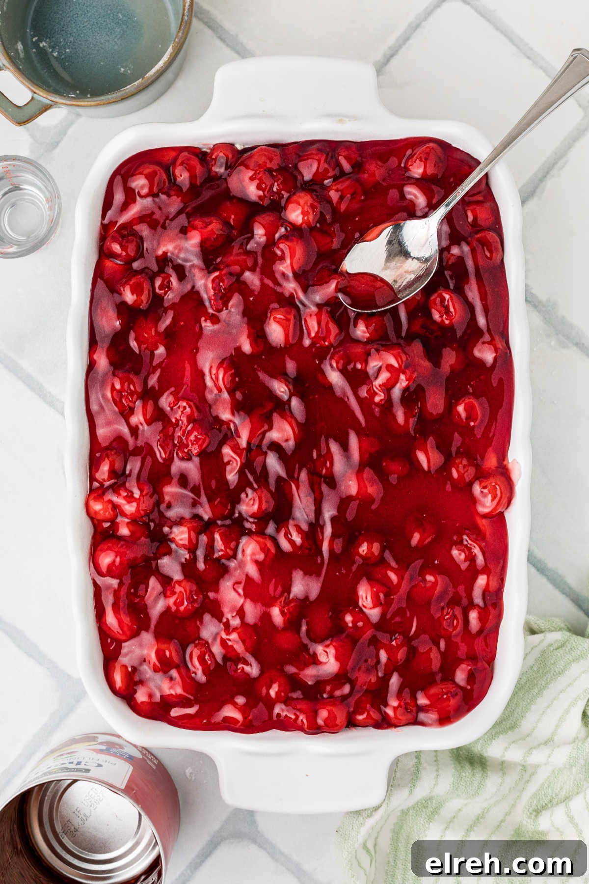 Cherry Pie filling being spread on top of a cream cheese layer.
