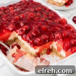 A dish with old fashioned cherry delight, with some squares missing and a spatula laying inside.