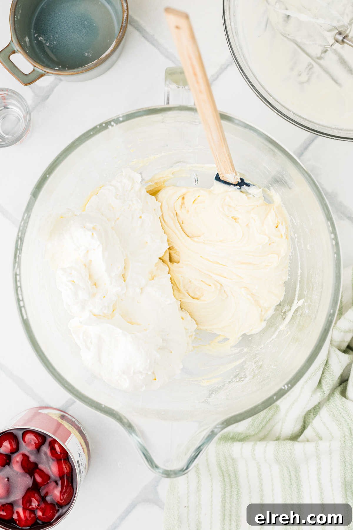 A mixing bowl with whipped cream being mixed with cream cheese.