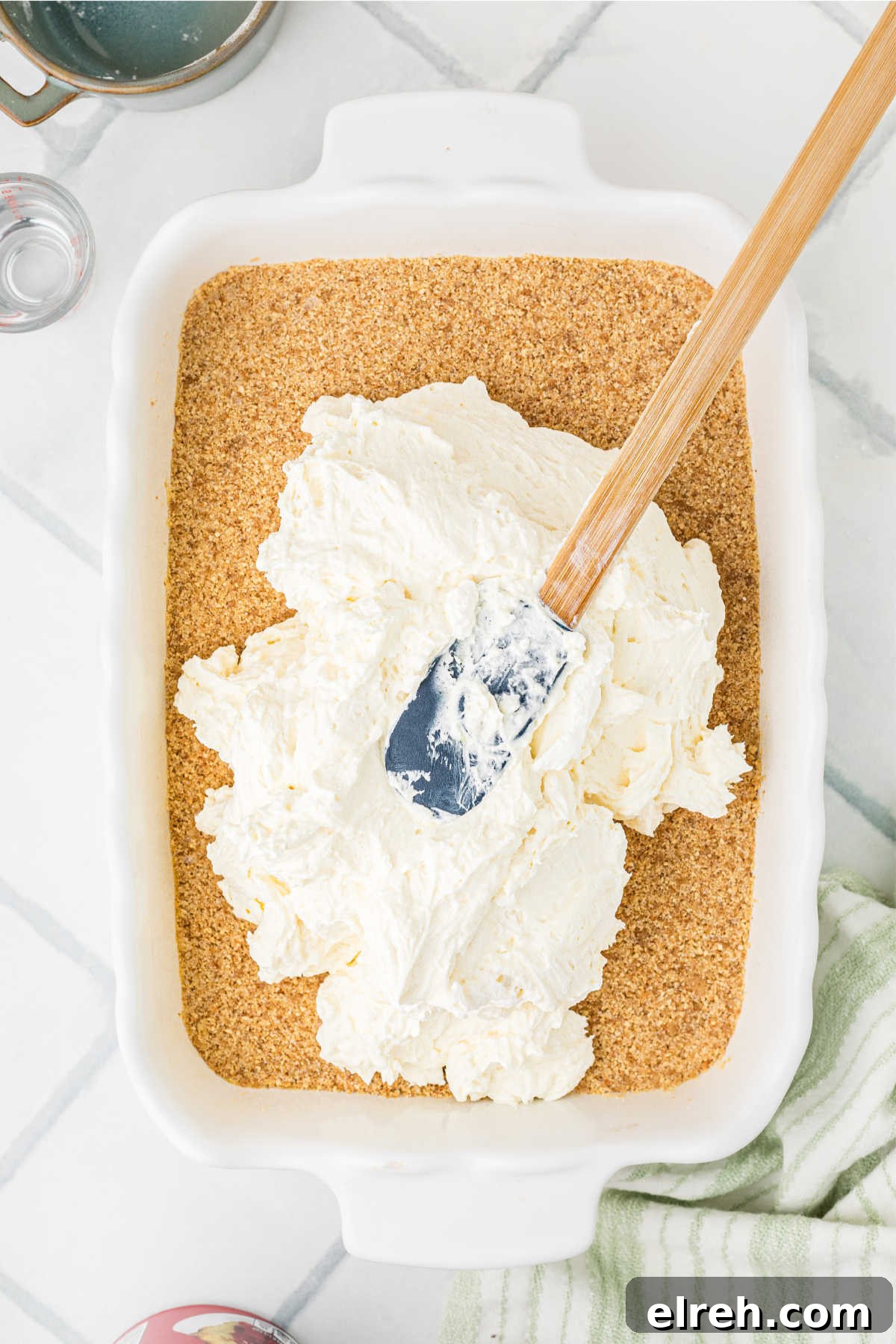 A cream cheese mixture being spooned on top of a crumb base.