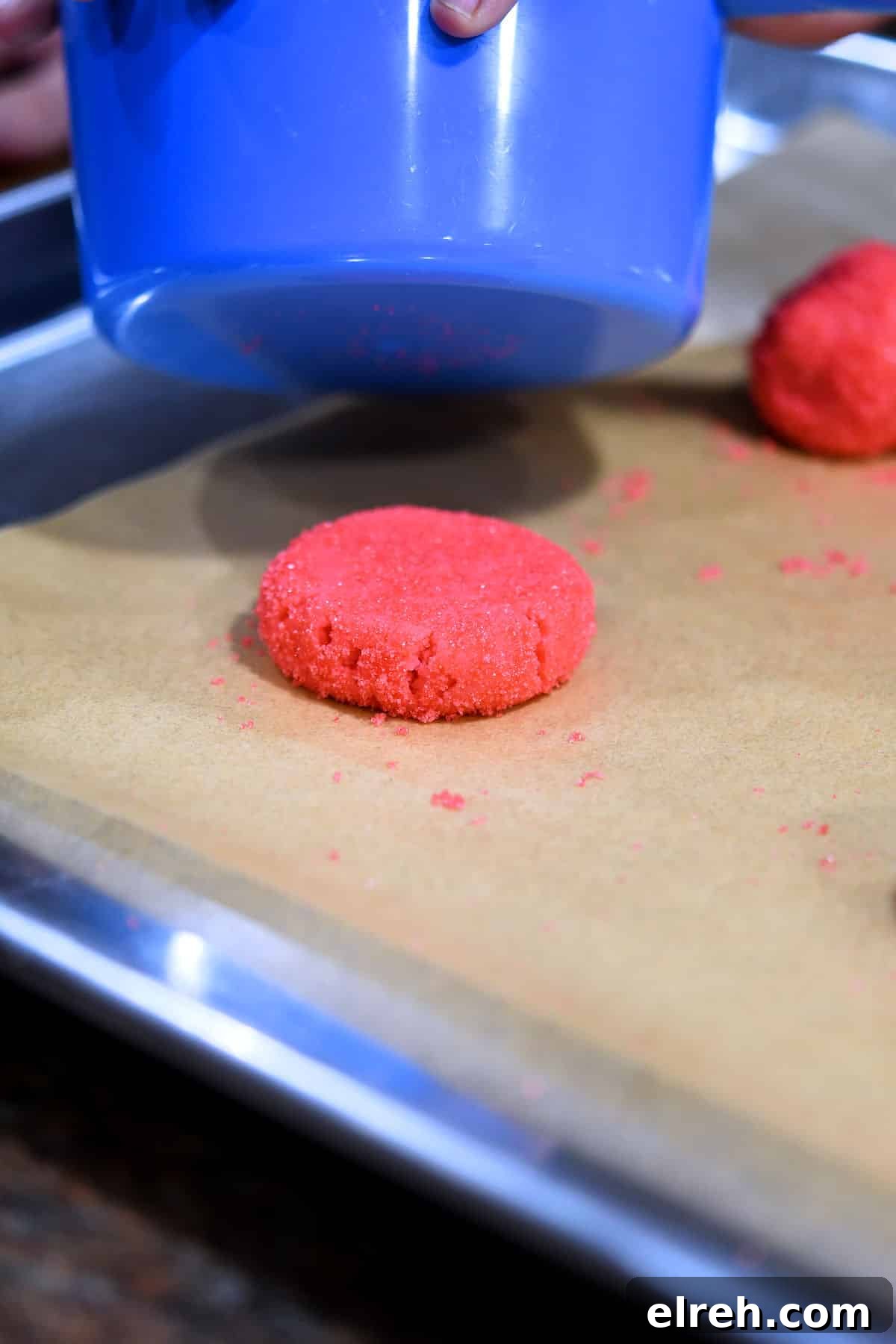 a ball of pink cookie dough being flattened with a measuring cup