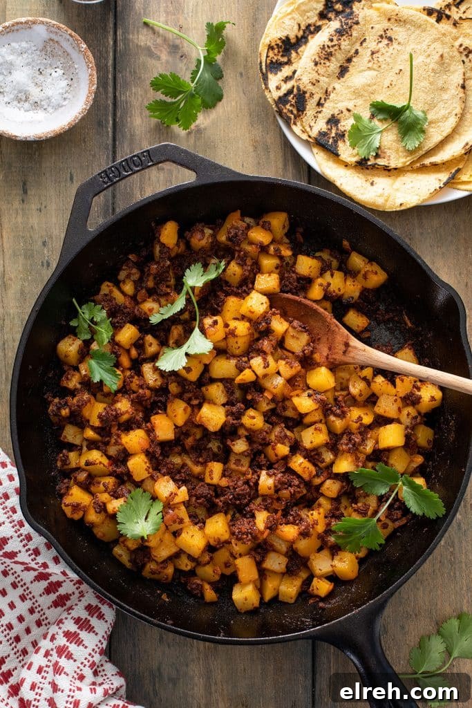 A cast iron skillet with a wooden spoon serving potatoes and Mexican chorizo