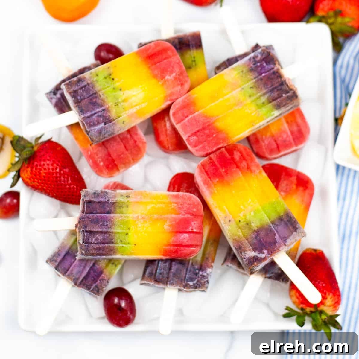 Rainbow popsicles served on a white platter garnished with strawberries and grapes