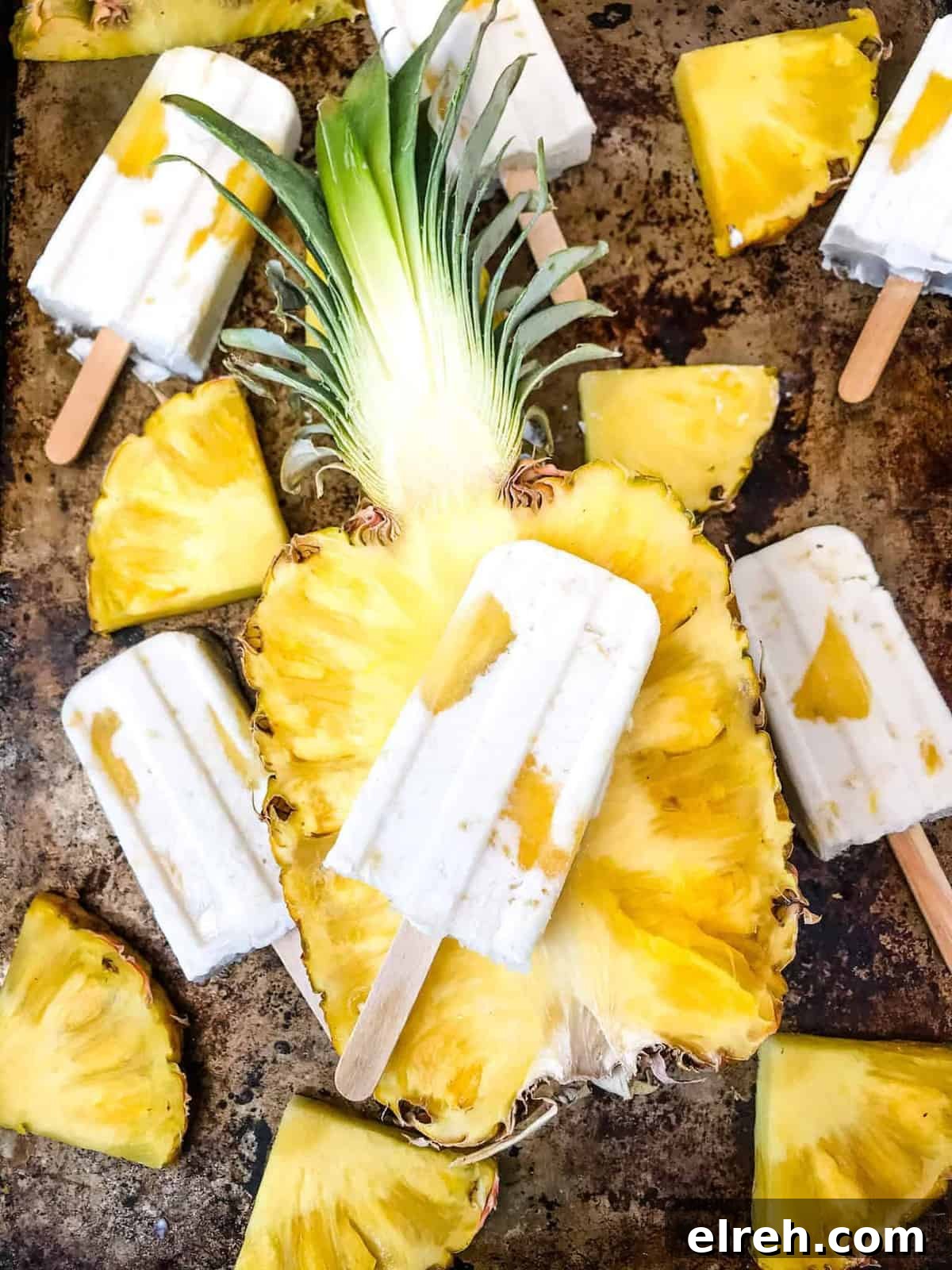 Pina colada popsicles on tray with pineapple.