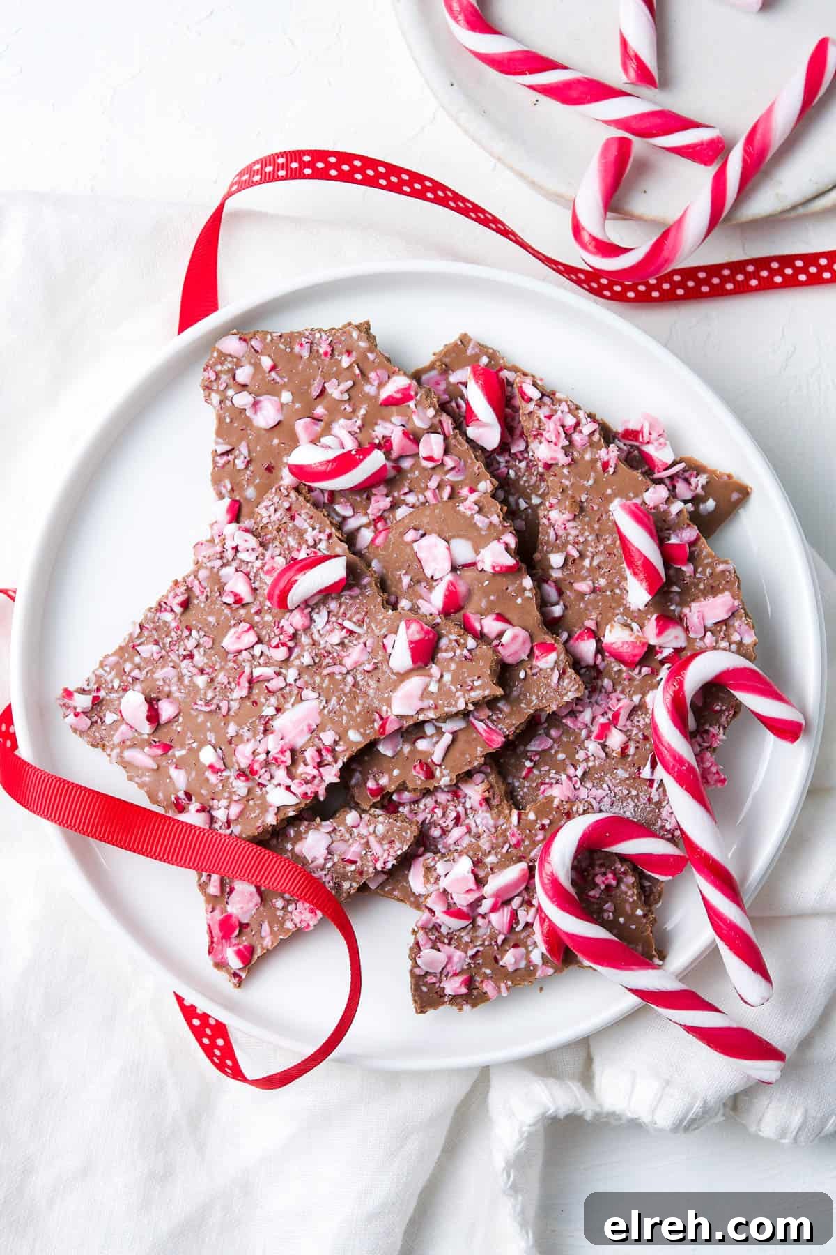 Chocolate Bark on a round white plate, decorated with some candy canes and some red ribbon.