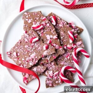 Round white dish of Candy Cane Chocolate Bark, with some red ribbon and additional candy canes on the edge.