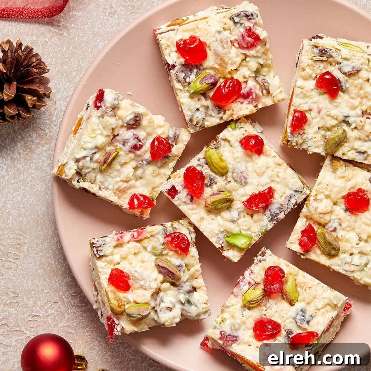 Round pink plate with squares of White Christmas Slice on it, and a couple of Christmas baubles and pine cones around the edge.