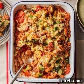 A big pan of baked tuna with pasta, cheese on top and vegetables, a portion having been served.