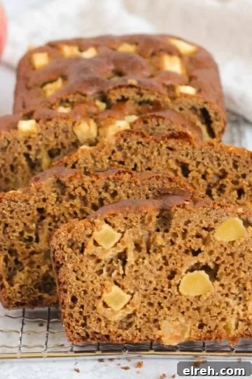 Slices of healthy apple bread on a rectangular wire cooling rack with a gold knife on the side and apples in the background.