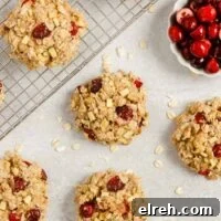 Multiple cranberry apple breakfast cookies spread out over a surface and cooling rack with a small dish of cranberries on the side.