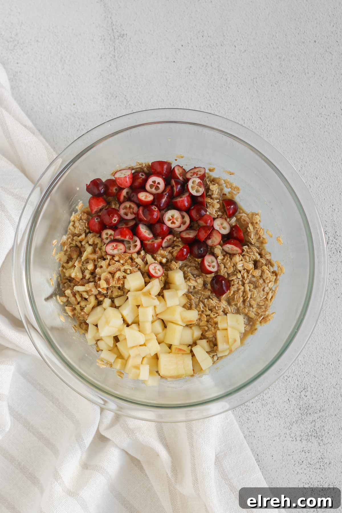 Cranberry Apple Breakfast Cookies Recipe 6 Oatmeal breakfast cookie dough in a glass mixing bowl with cranberries, apples, and walnuts added to the top.