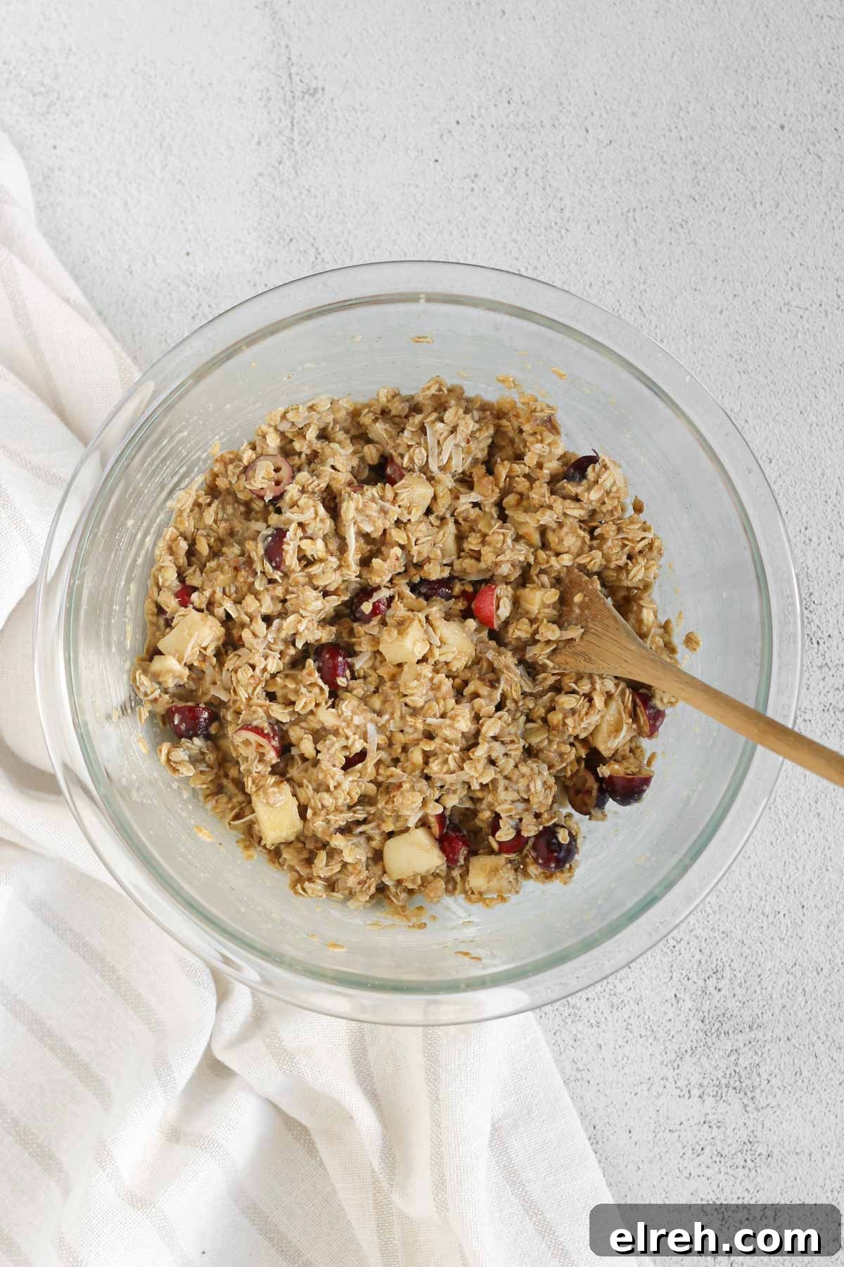 Cranberry Apple Breakfast Cookies Recipe 7 Cranberry apple breakfast cookie ingredients all mixed in a glass mixing bowl with a wooden spoon.