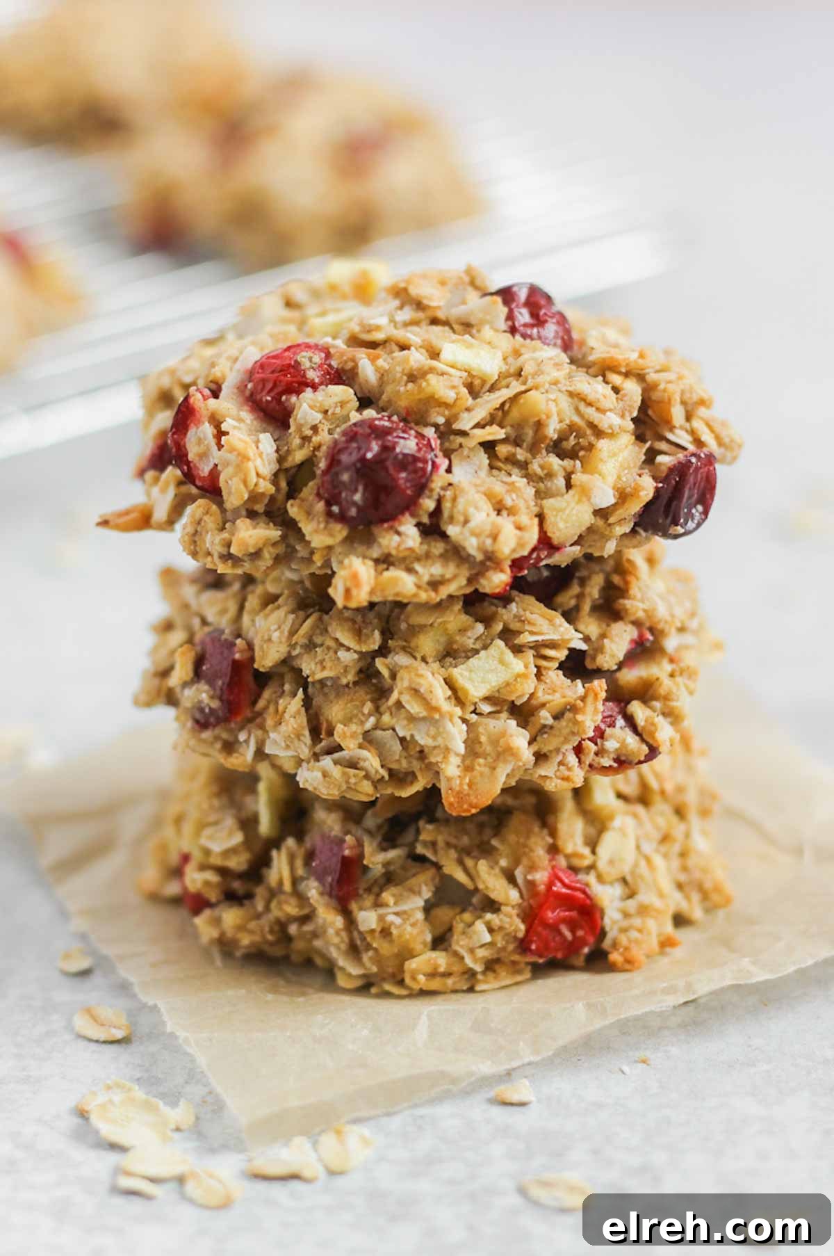 Cranberry Apple Breakfast Cookies Recipe 10 Three cranberry apple oatmeal breakfast cookies stacked on top of each other on a square piece of parchment paper.