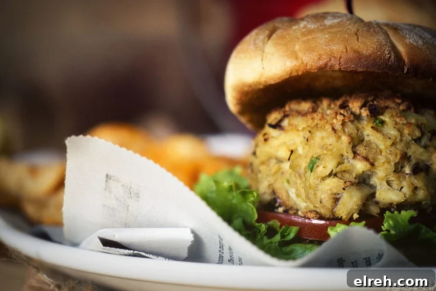 Side shot of a crab cake sandwich, a thick maryland crab cake atop lettuce and tomato. 