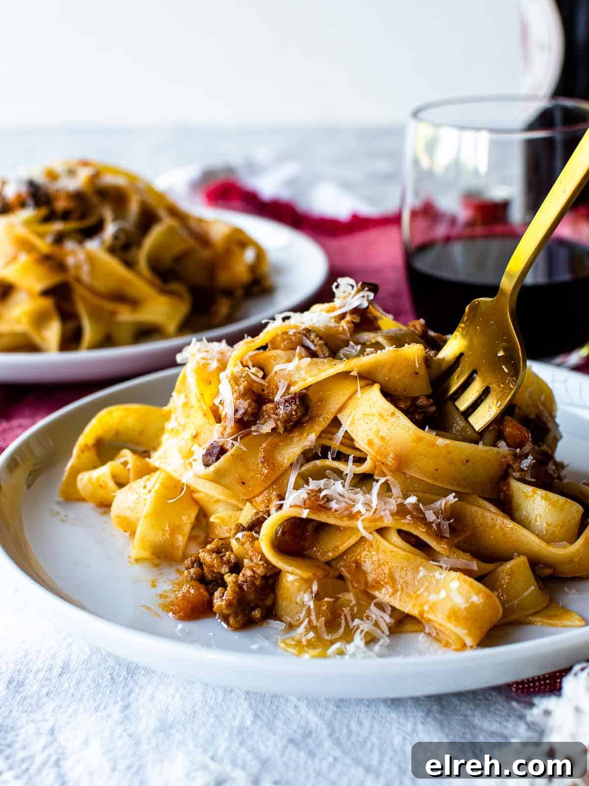 Authentic Tagliatelle with Bolognese Sauce Recipe 2 White plate with tagliatelle alla bolognese pasta on it and a gold fork in the pasta.