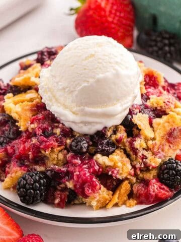 Berry cobbler with cake mix topped with vanilla ice cream on a plate with fresh berries nearby.