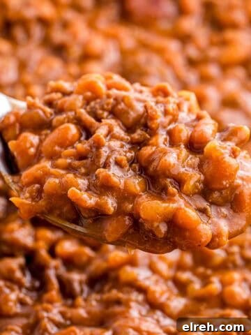 Spoonful of baked beans with ground beef held above the dish to show the thick texture and rich sauce.