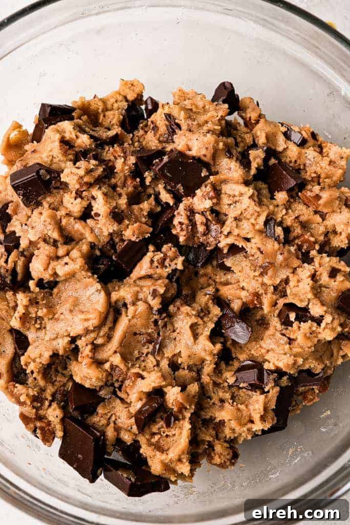 A glass bowl filled with thick cookie dough studded with chocolate chunks and pieces of toffee.