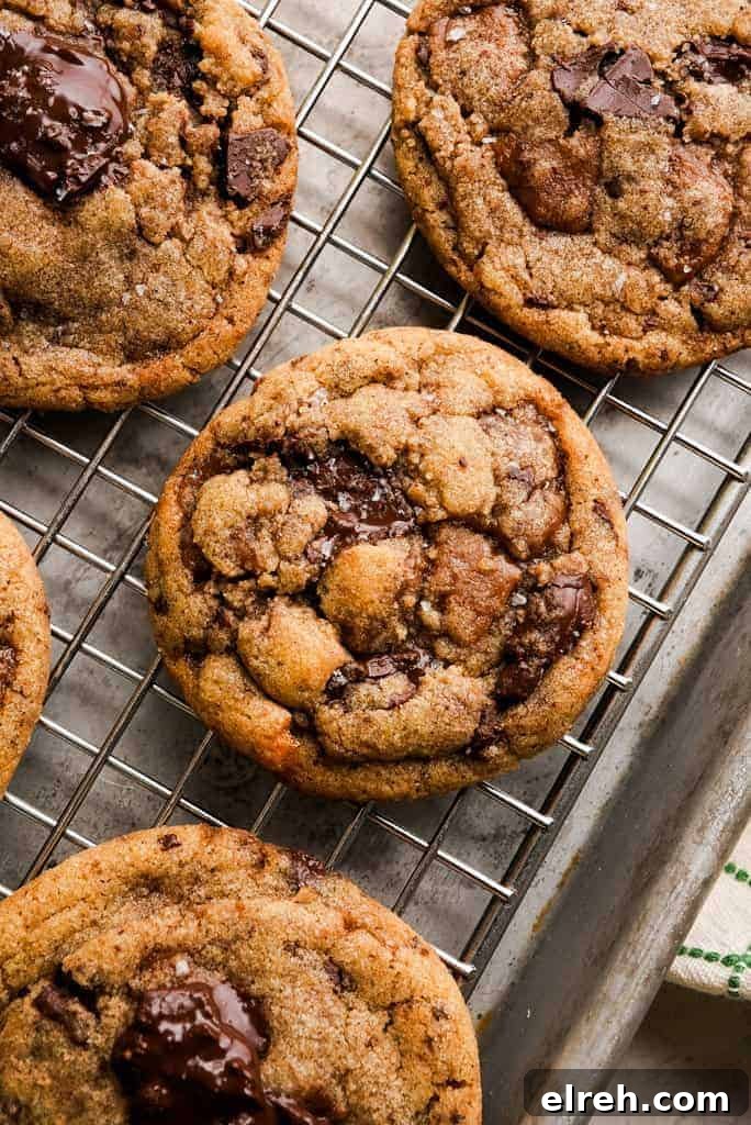 Several baked brown butter toffee chocolate chip cookies with cracked tops and visible chocolate chunks rest on a wire cooling rack.