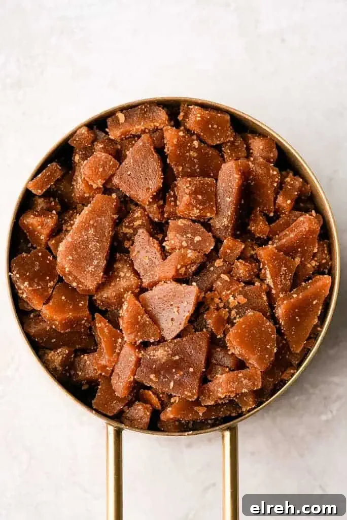 A gold measuring cup filled with broken pieces of amber colored toffee sits against a light background.