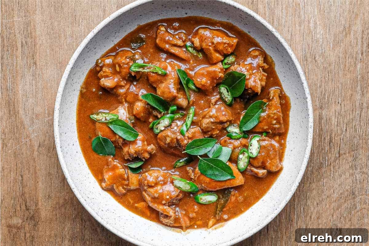 A bowl of Chicken Ceylon Curry scattered with fresh curry leaves and green chillies