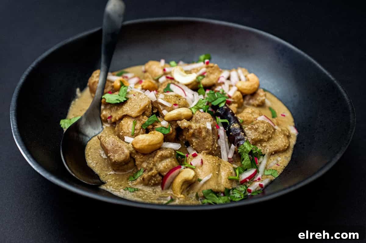 Bengali Rezala Chicken in a black bowl with spoon on a black background.